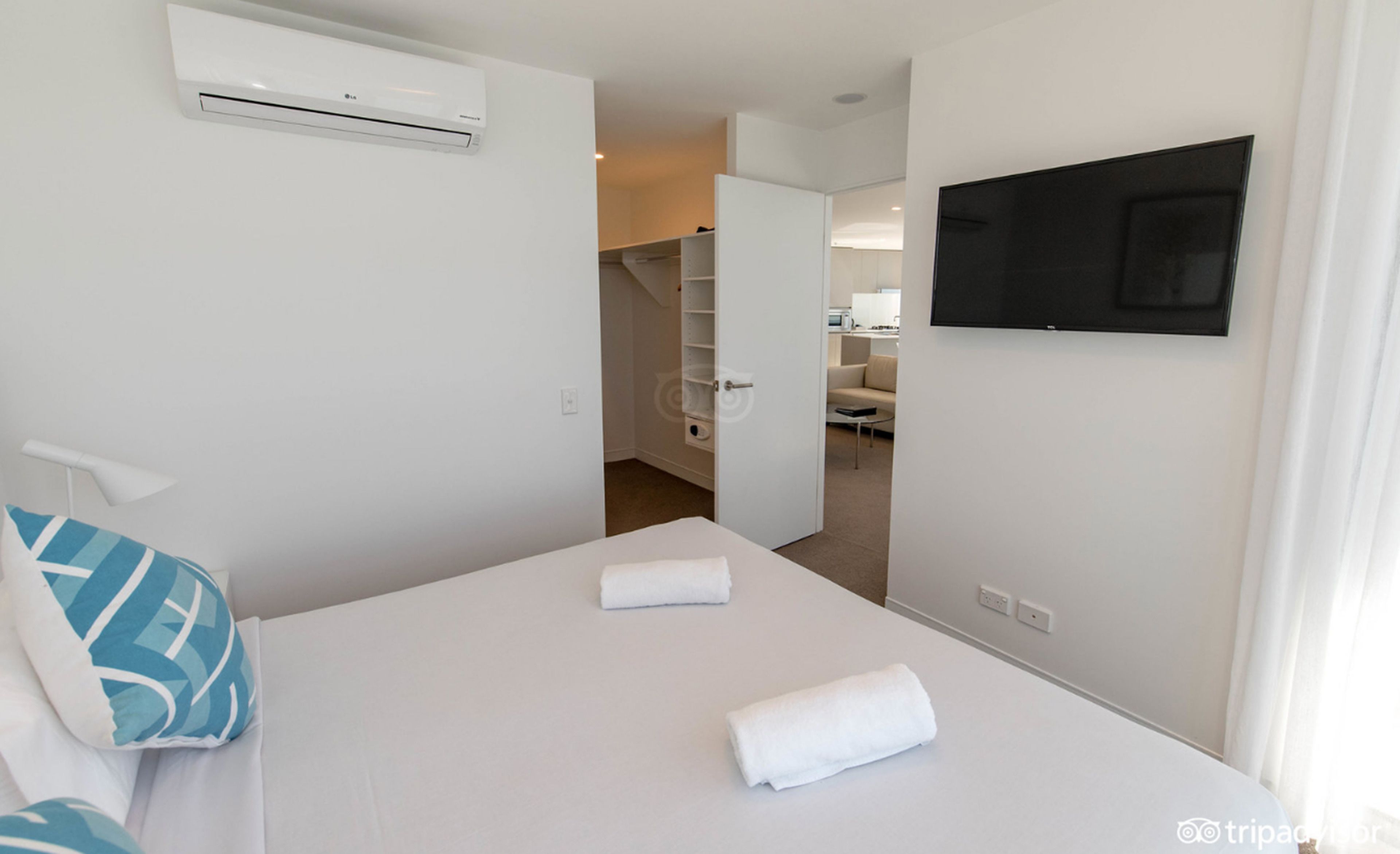 Una habitación de hotel con una cama, un televisor montado en la pared y un equipo de aire acondicionado sobre la cama.