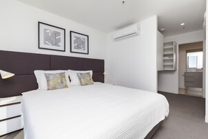 Quarto moderno com cama grande, cabeceira escura, duas obras de arte emolduradas, abajur e armário embutido.