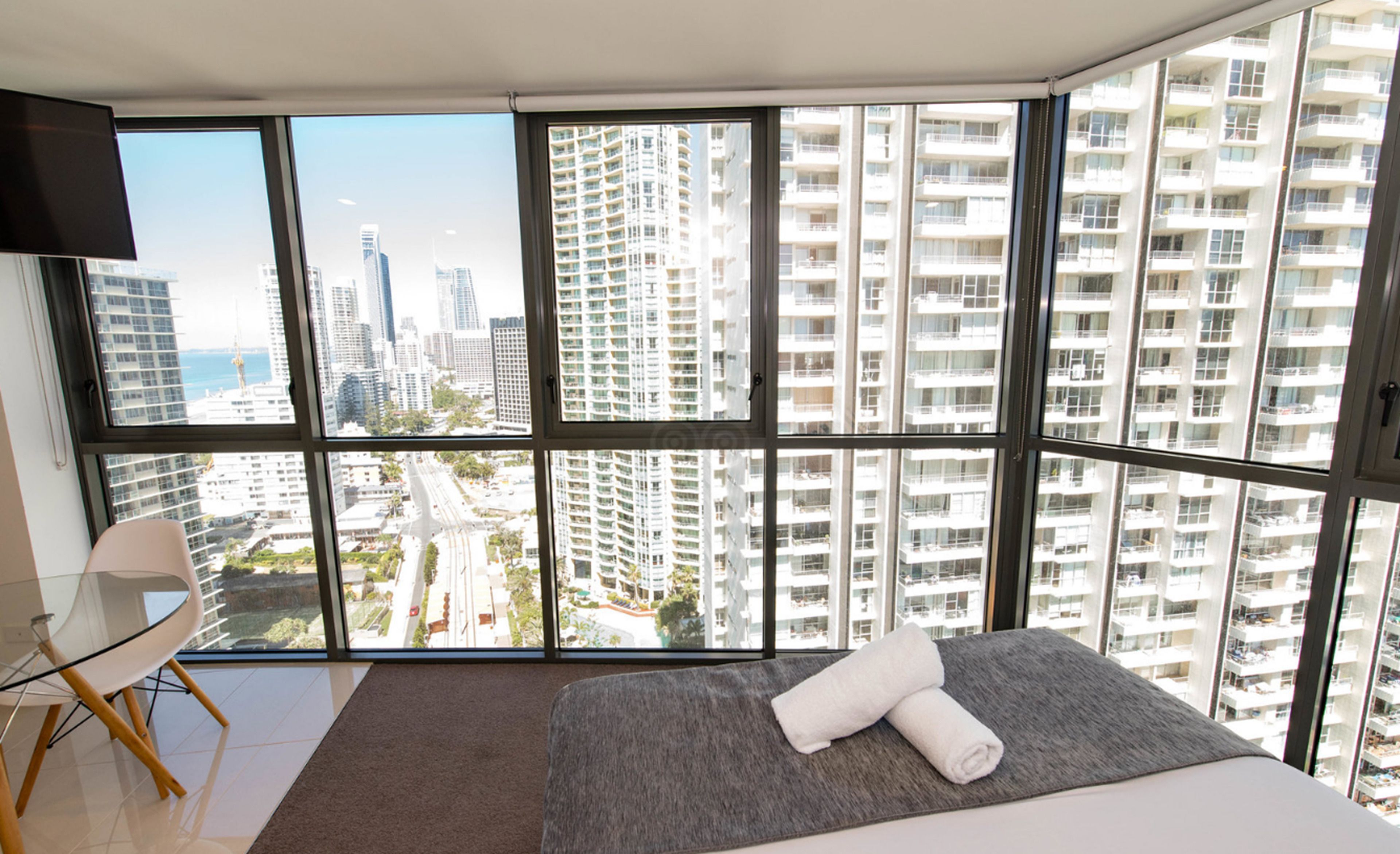 Una habitación de hotel moderna con un ventanal grande, una cama, una silla y un televisor de pantalla plana.