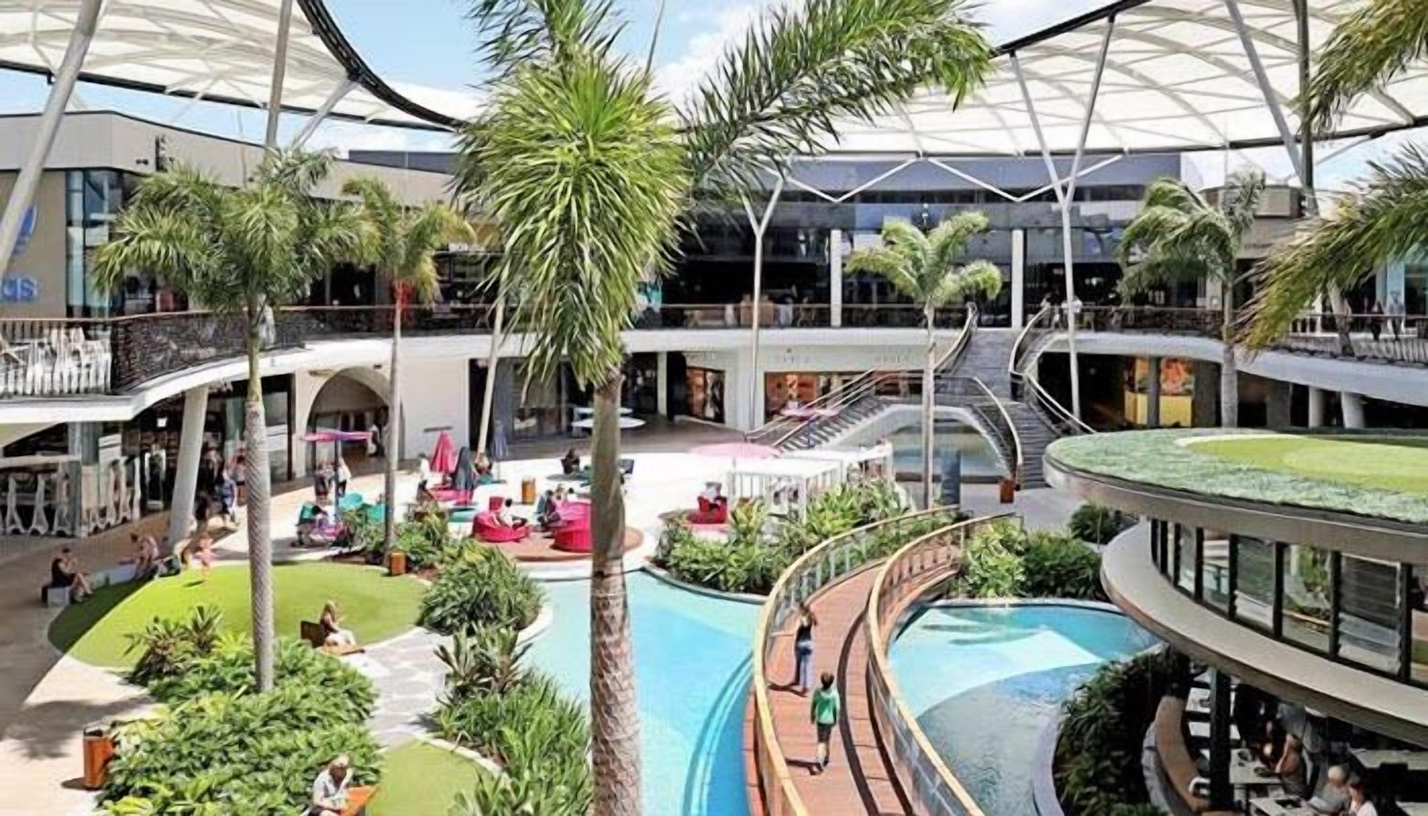 A multi-level indoor space with a central pool, palm trees, and a covered area with seating.