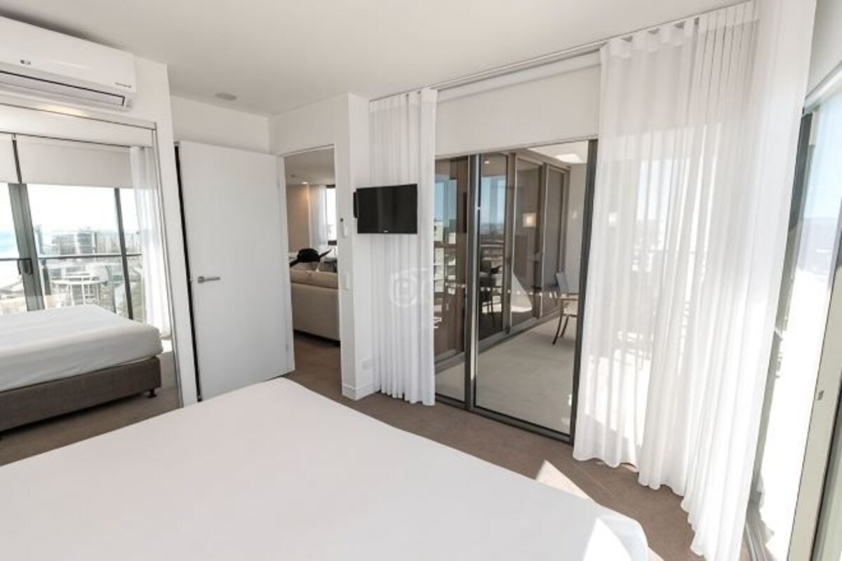 Une chambre d’hôtel avec un lit, une télévision, une porte-fenêtre coulissante donnant sur un balcon et une vue sur la ville.