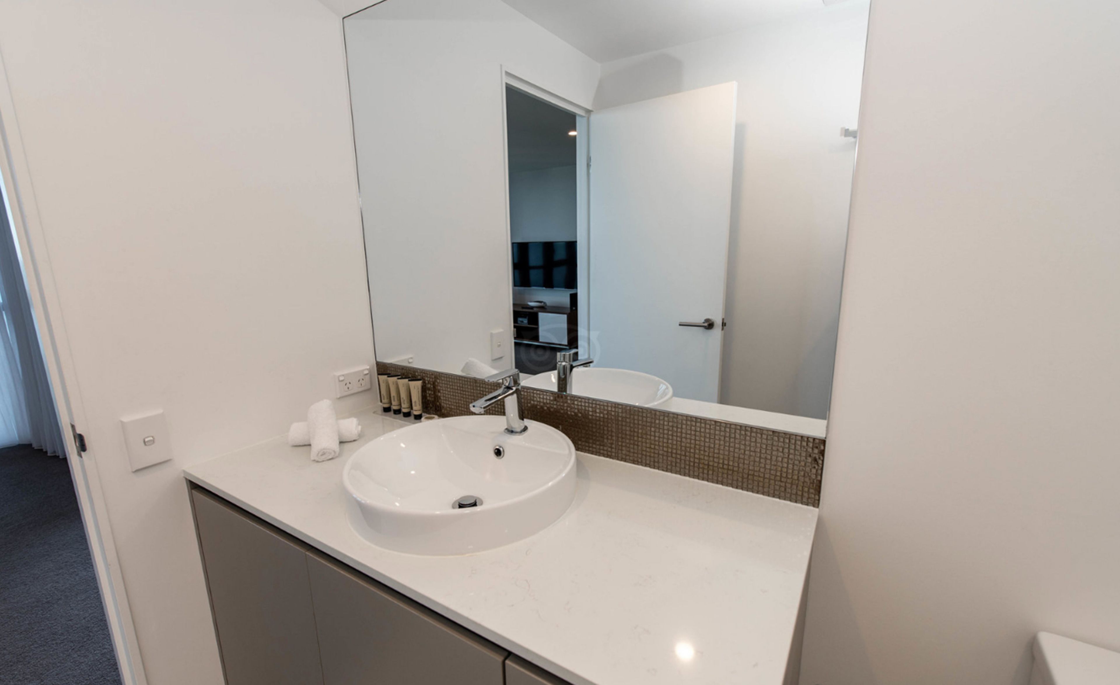 A modern bathroom with a white sink, a large mirror, and a towel rack.