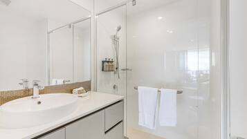 A modern bathroom with a large white sink, a glass shower enclosure, and a mirror.