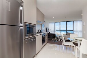Una cocina moderna con electrodomésticos de acero inoxidable, un comedor con mesa de vidrio y vista al océano a través de amplios ventanales.