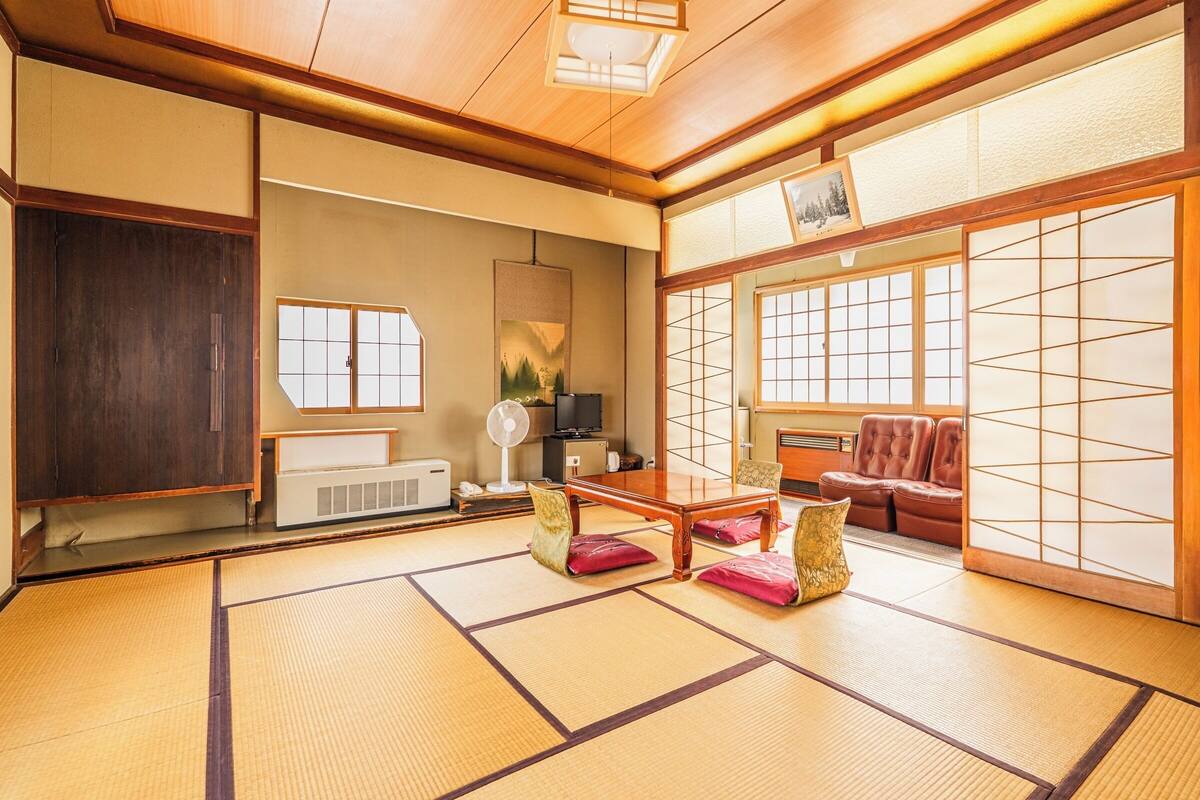 A traditional Japanese room with tatami flooring, a tatami mat table, a wooden cabinet, a tatami mat sofa, and a sliding shoji screen.