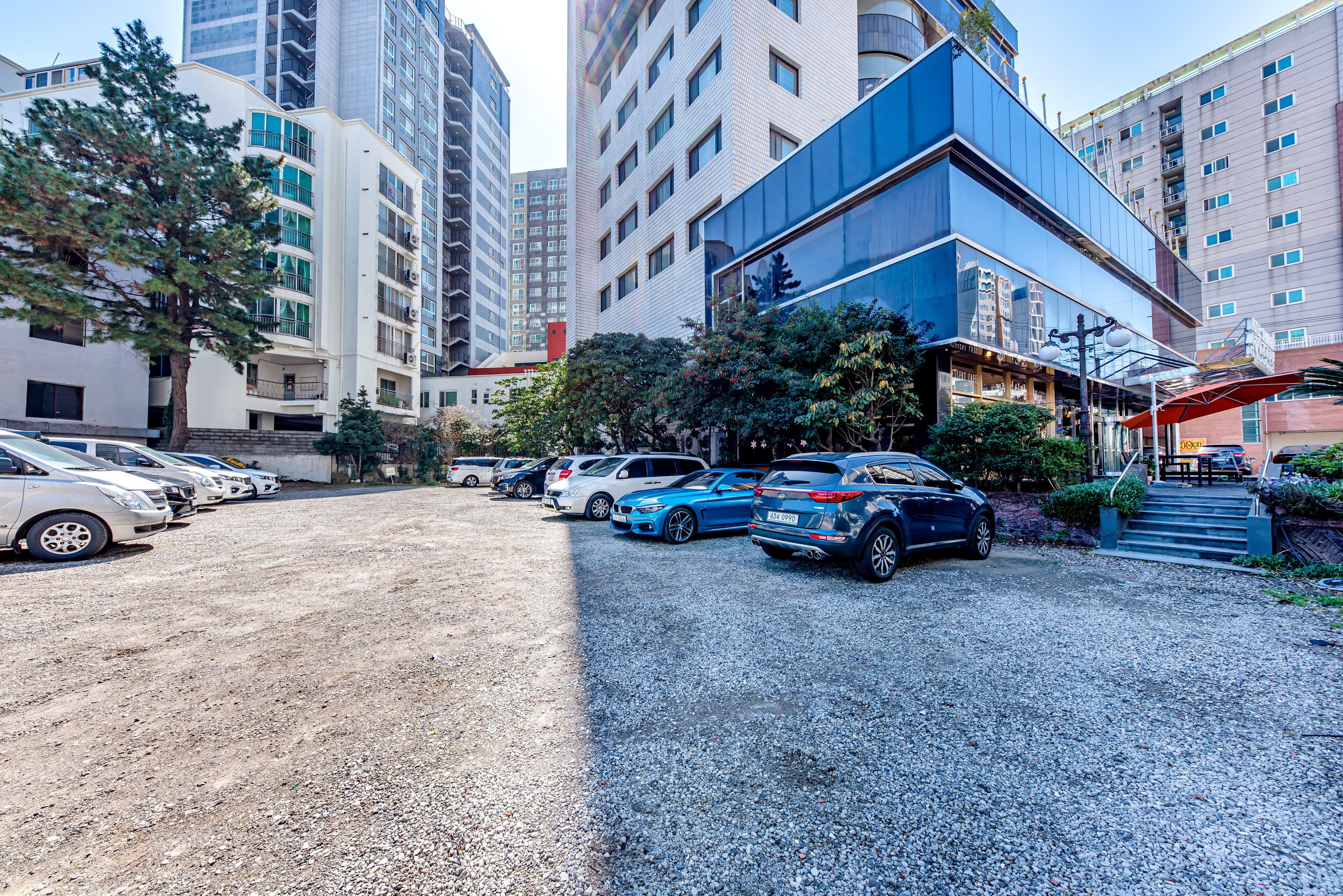 A parking area with multiple cars, a building with a modern design, and a staircase leading to an entrance.