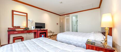 A hotel room with two beds, a desk, a TV, and a lamp.