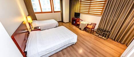 A hotel room with two beds, a TV, a desk with a chair, and a shoe rack.
