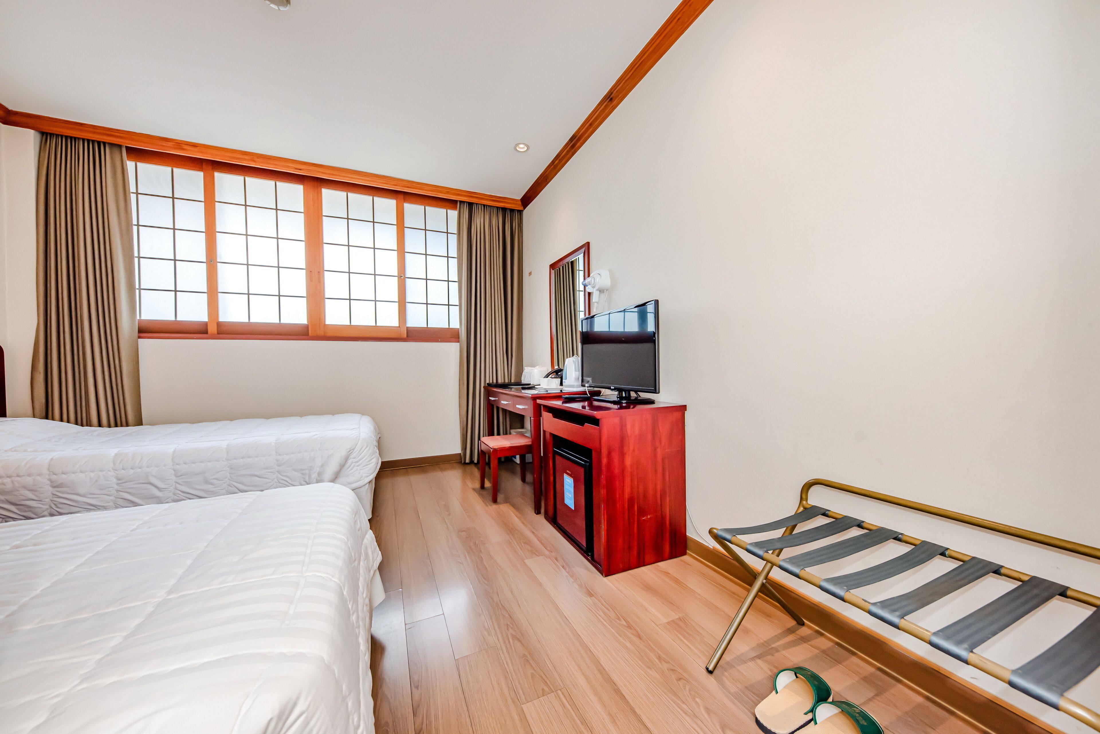 Habitación de hotel con dos camas, un escritorio con televisor y una ventana con cortinas.