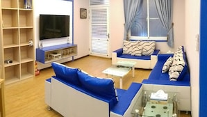 A modern living room with a flat-screen TV, blue sofas, a glass coffee table, and a bookshelf. - Simple Travel - Hostel (Donggang)