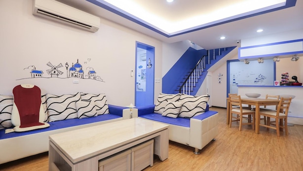 A modern living room with a sofa, a coffee table, a dining area with a table and chairs, a staircase, and a wall with a cityscape mural. - Simple Travel - Hostel (Donggang)