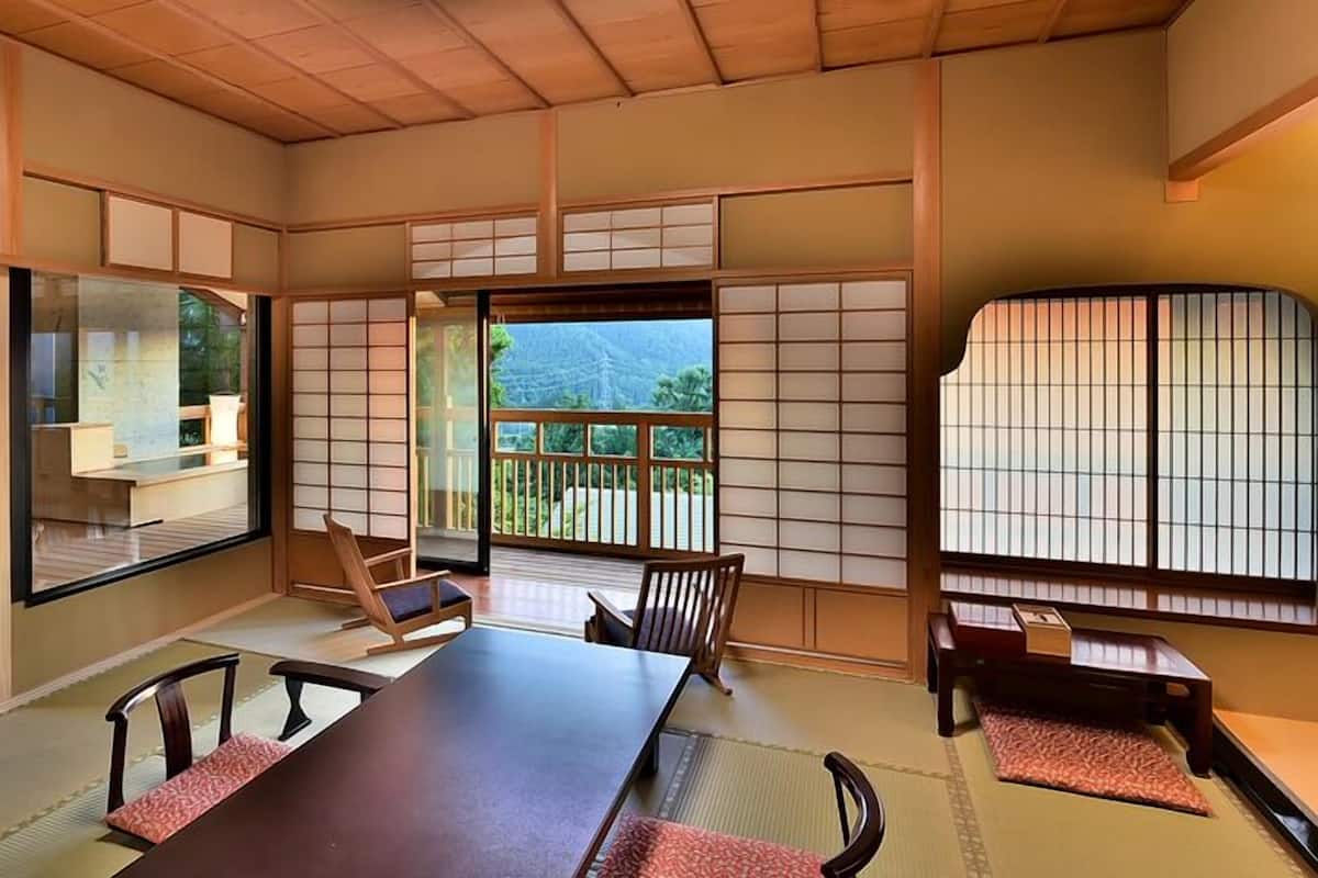 Een traditionele Japanse kamer met tatami vloeren, schuifdeuren en uitzicht op een bergachtig landschap.
