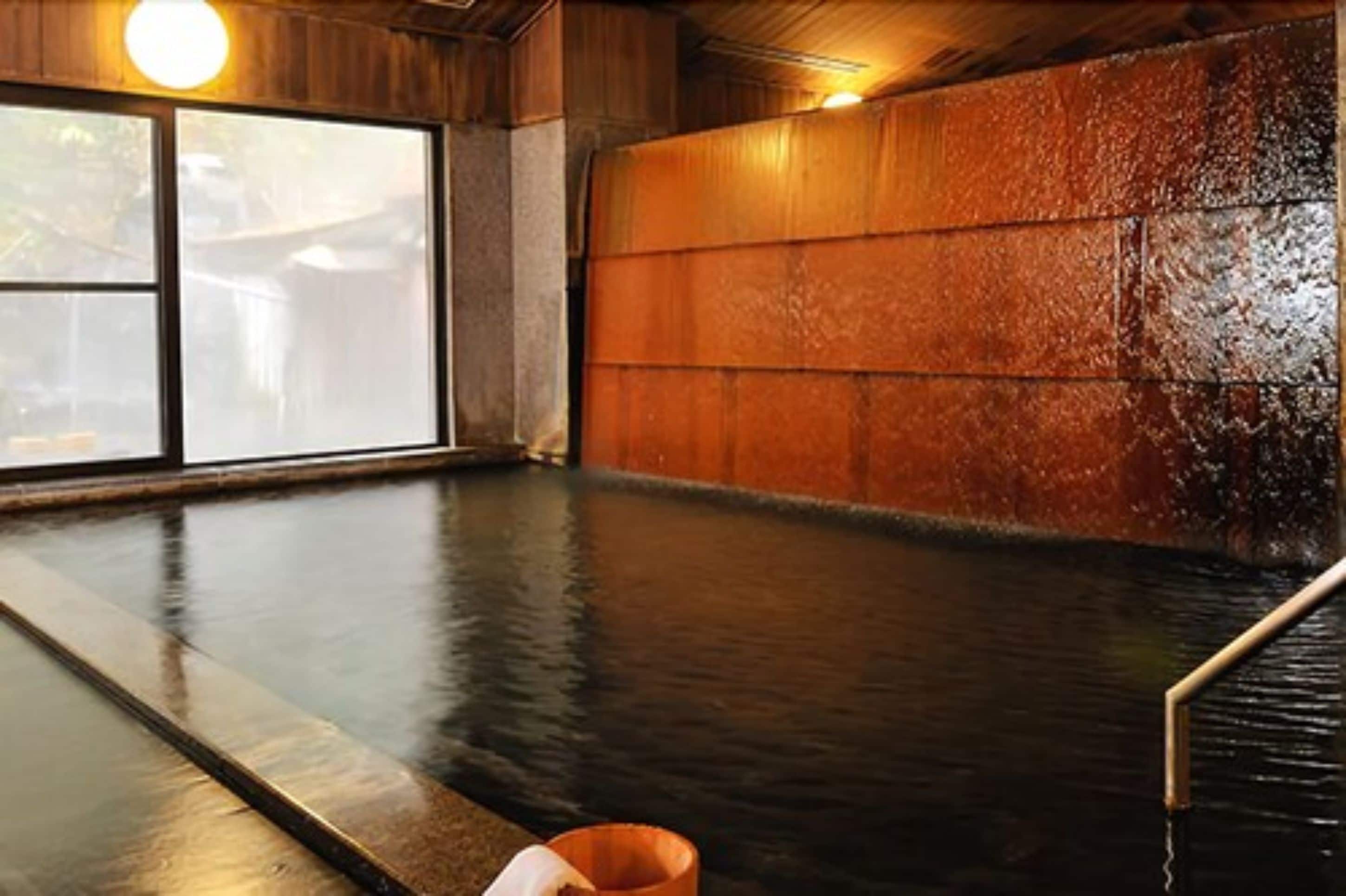 A traditional Japanese onsen with a wooden interior, a large window, and a stone wall.
