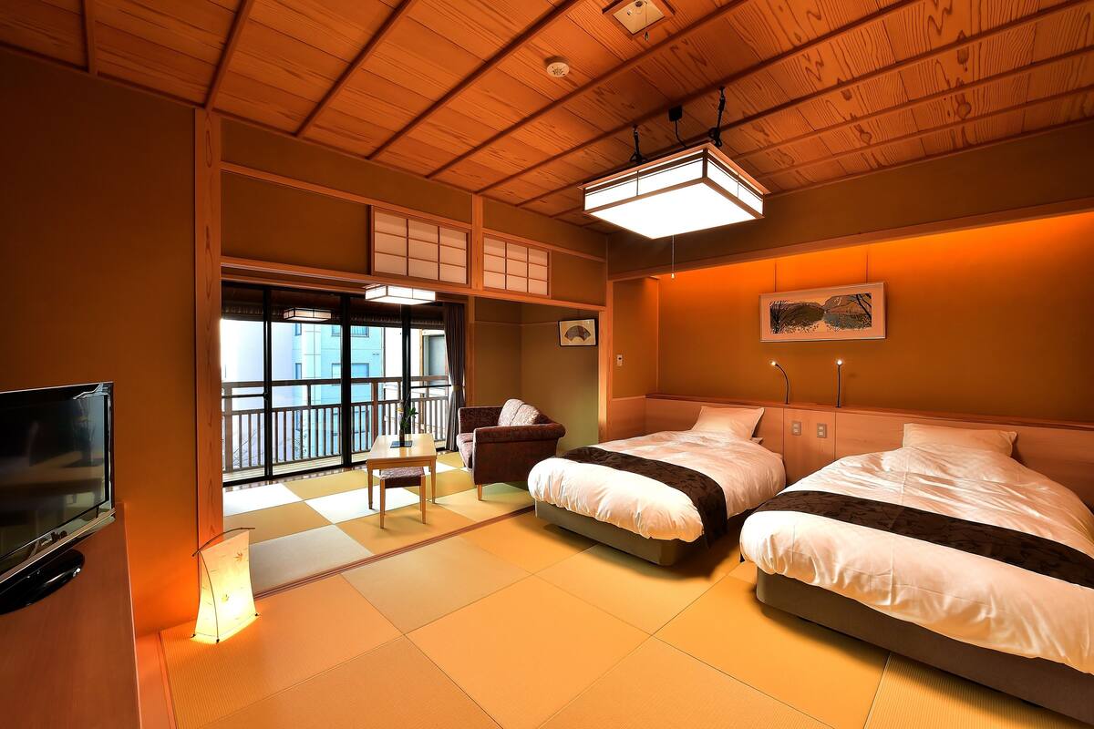 Hotelkamer met tatami vloer, een bed, een stoel, een televisie en een balkon met uitzicht.