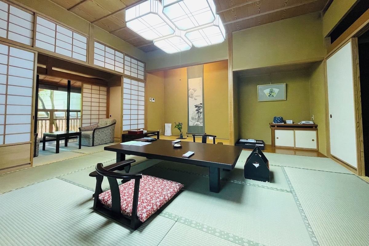 Een traditionele Japanse kamer met tatami vloerbedekking, een lage tafel met kussens en schuifdeuren.