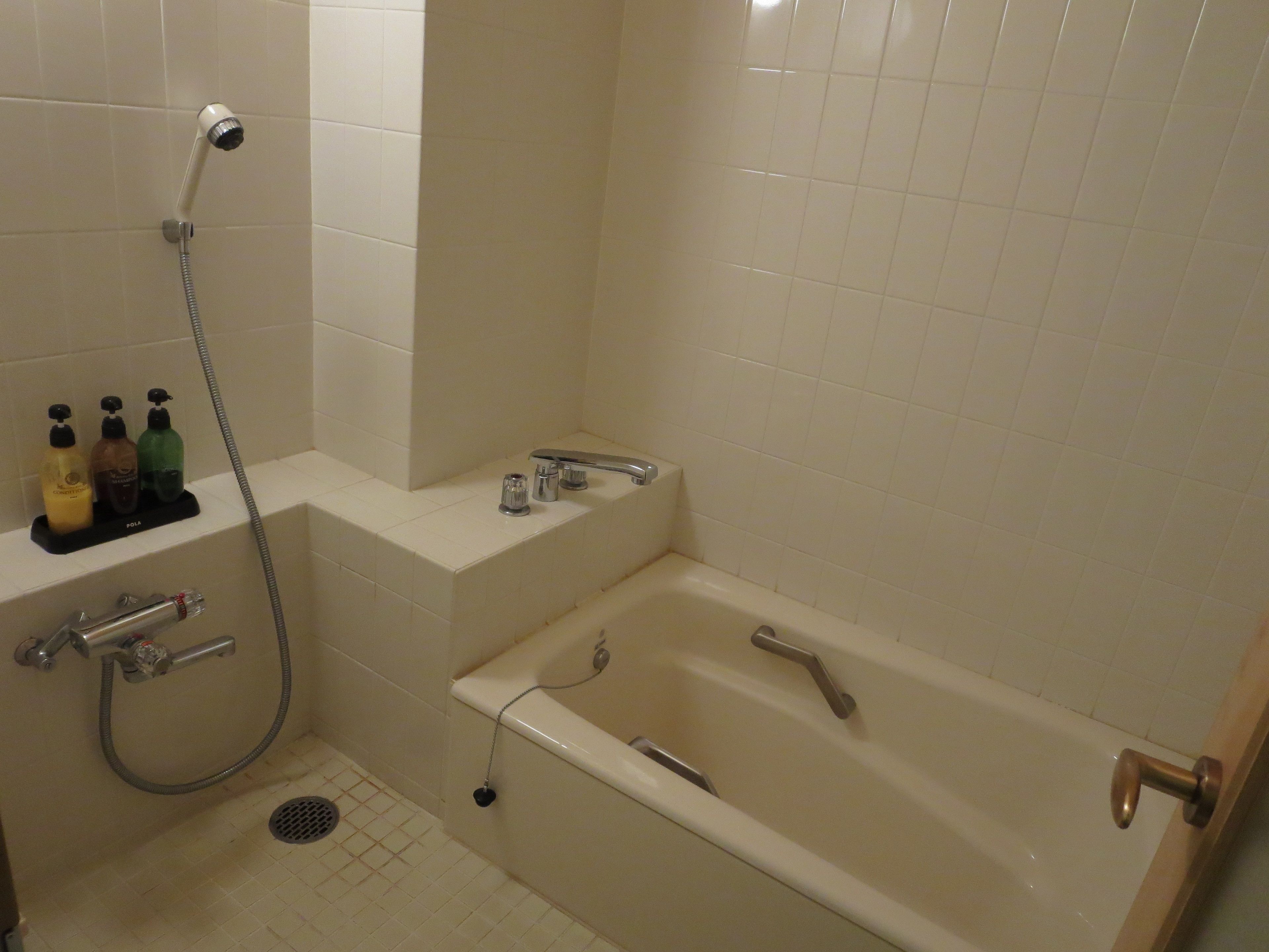 A bathroom with a bathtub, a shower, and a shelf with toiletries.