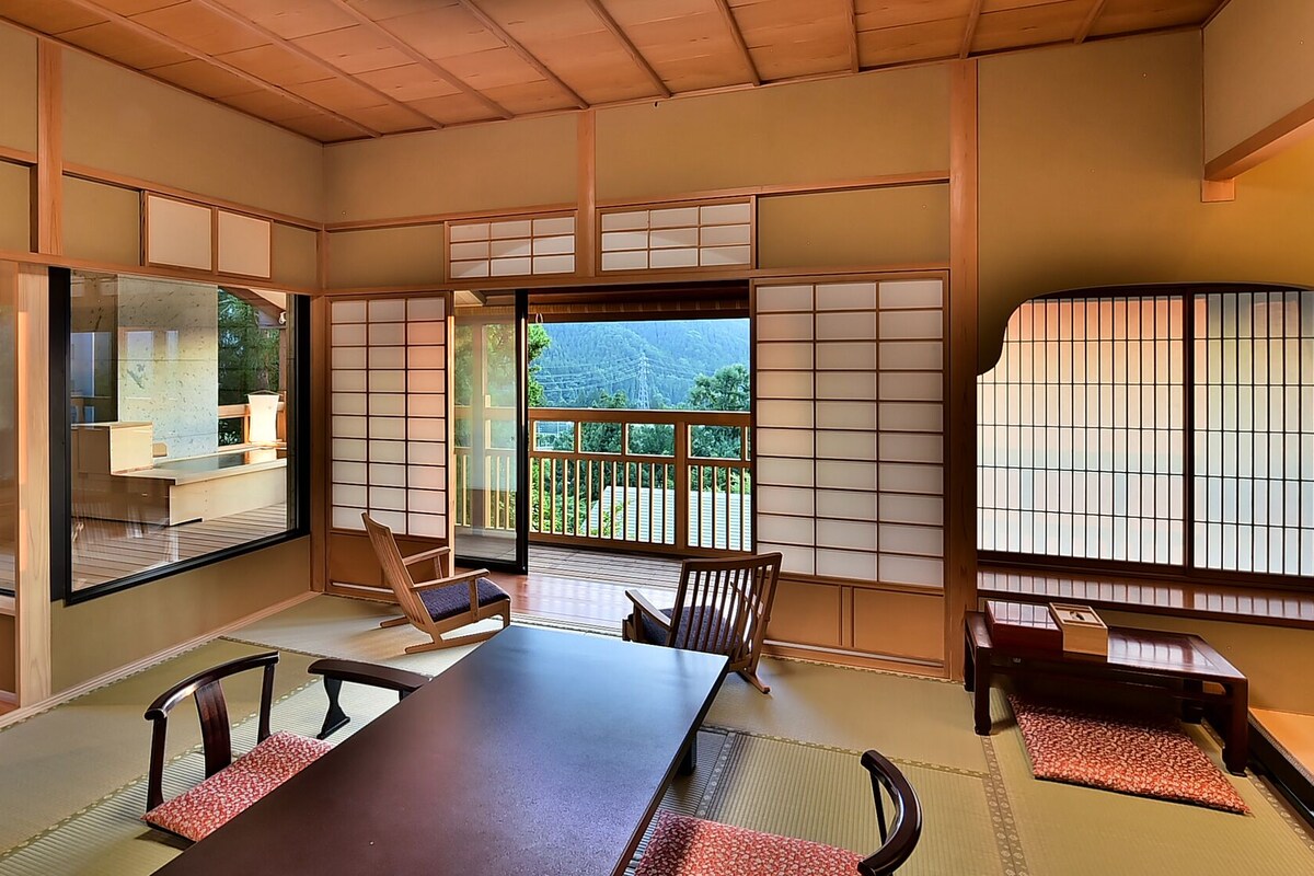 A traditional Japanese room with tatami flooring, sliding doors, and a view of a mountainous landscape.