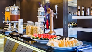 Um balcão de buffet com diversos alimentos, uma máquina de café e uma torneira de chopp.