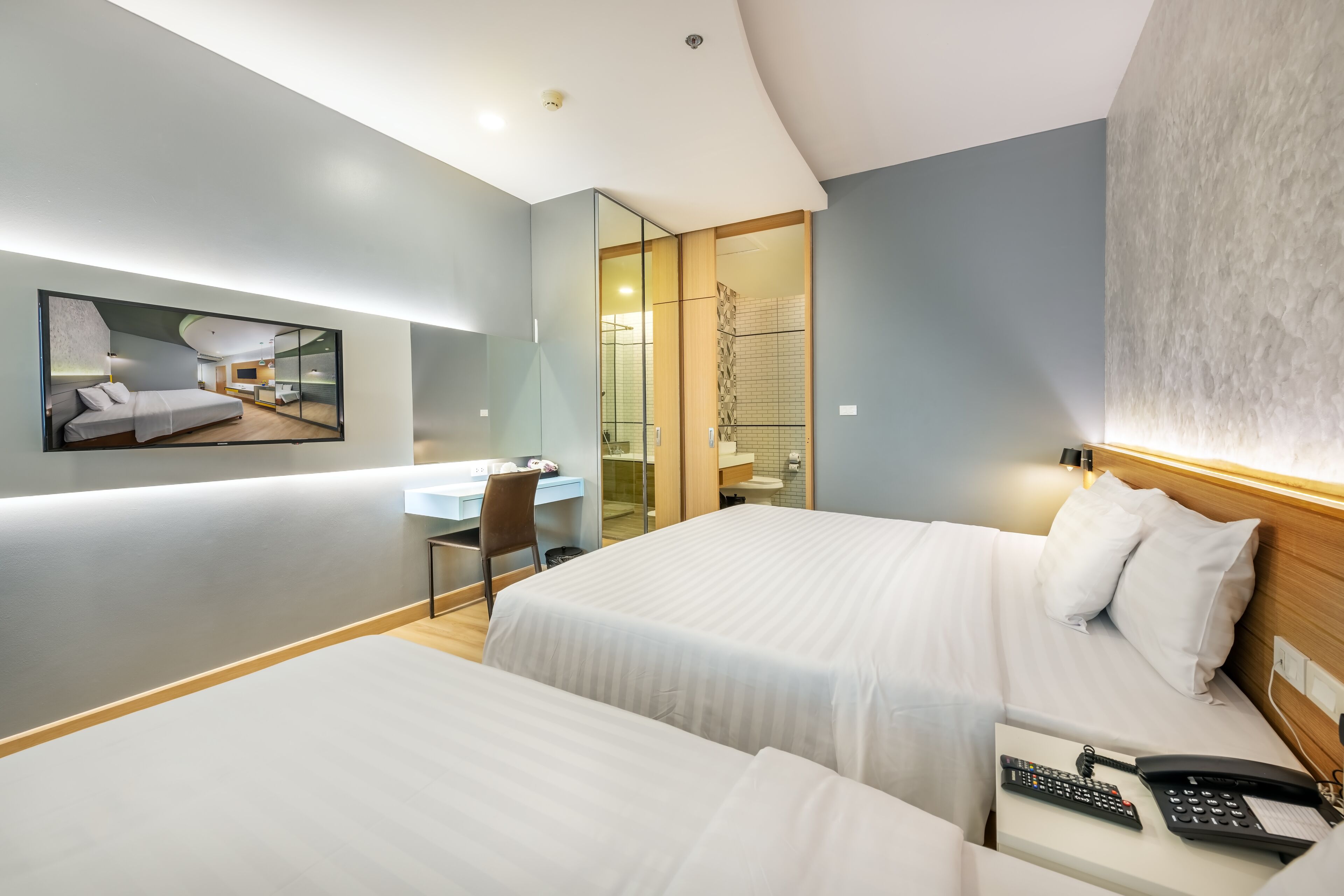 A hotel room with two beds, a desk, and a mirror.