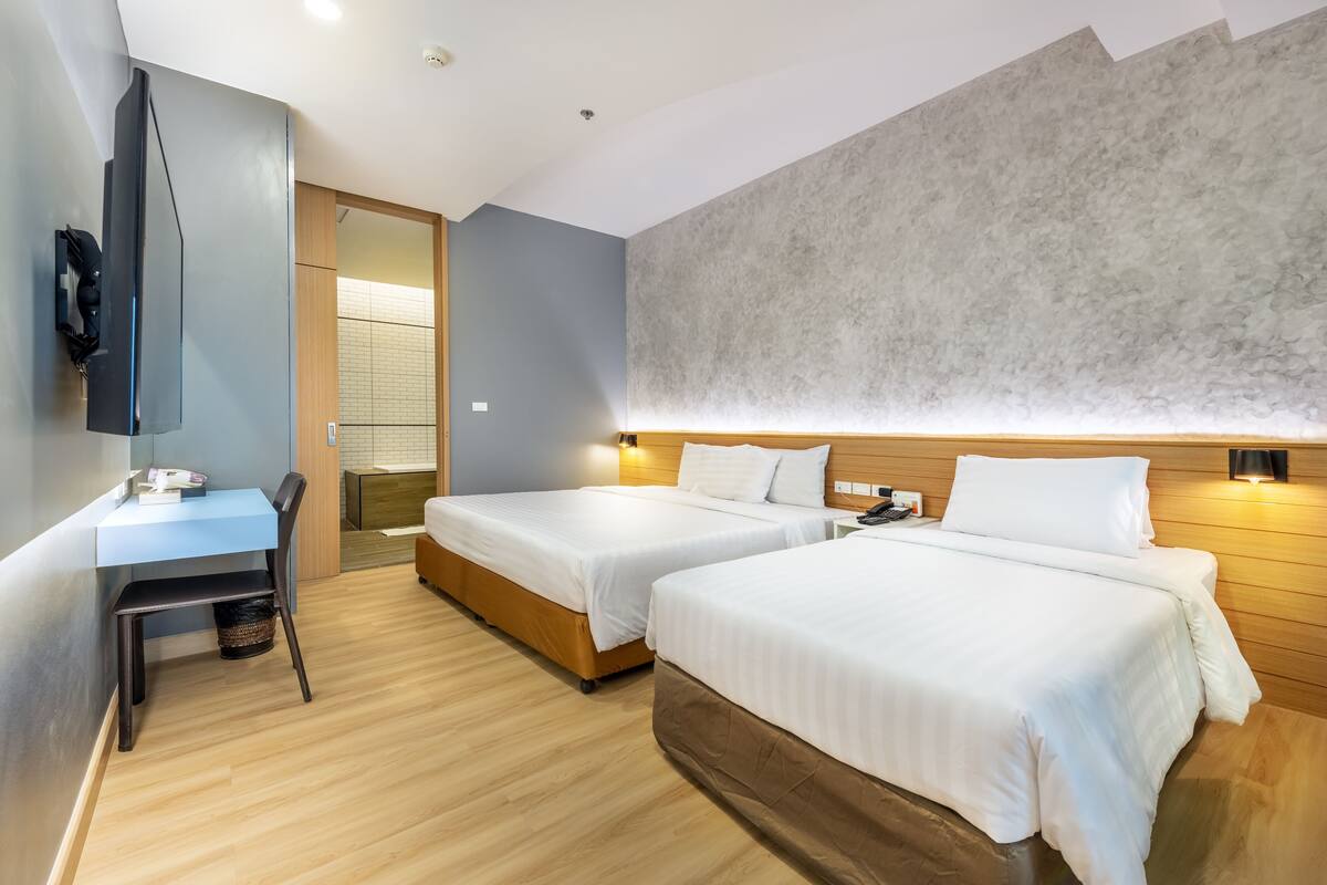 Habitación de hotel con dos camas, un escritorio, un televisor y un gran muro con textura.