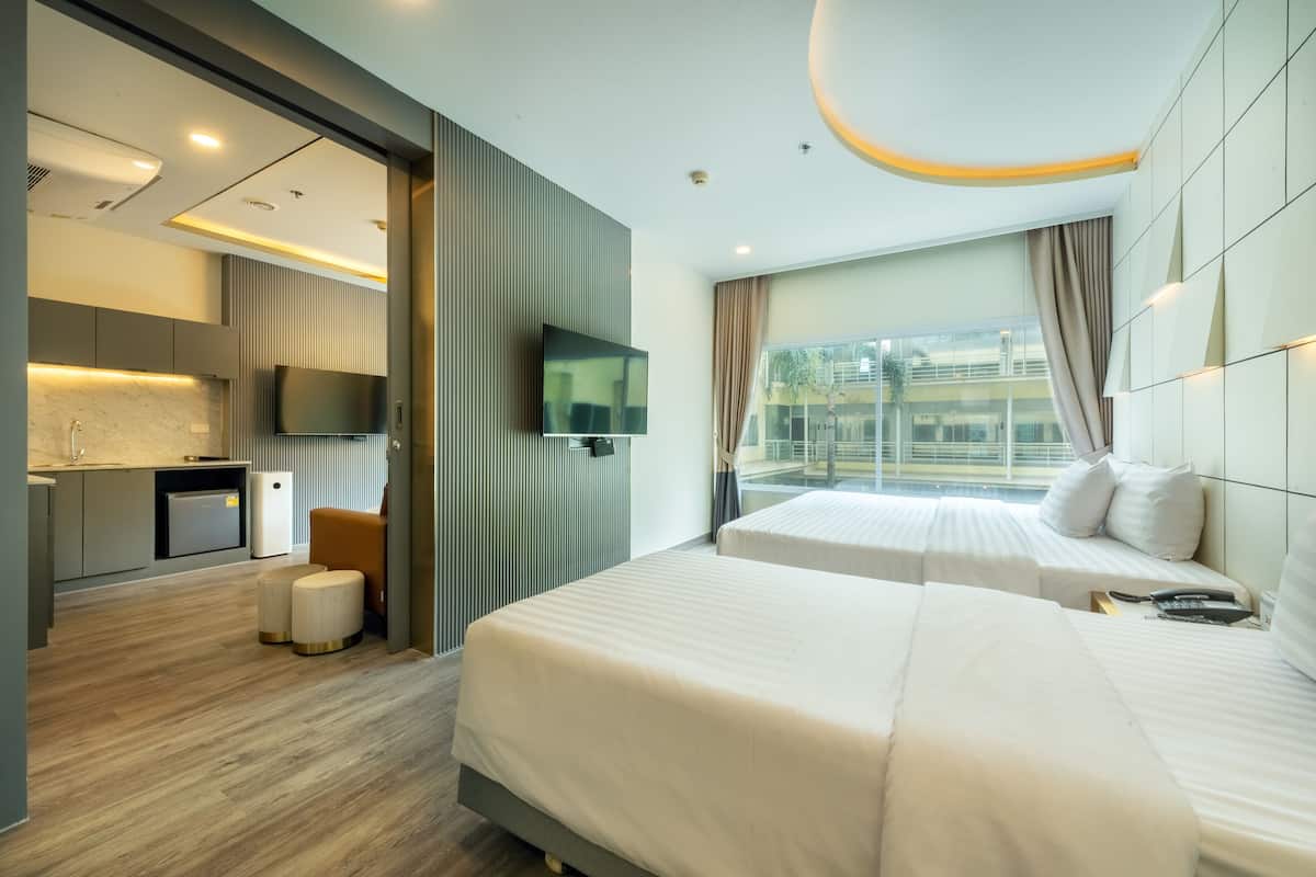 Habitación de hotel moderna con dos camas, televisión, kitchenette pequeño y un ventanal grande con cortinas.