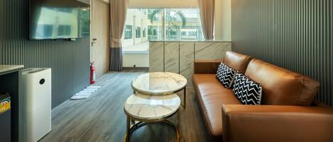 Une chambre d’hôtel moderne dotée d’une grande télévision à écran plat, d’un canapé agrémenté de coussins à motifs, d’une table basse en marbre et offrant une vue sur la ville grâce à de grandes fenêtres.