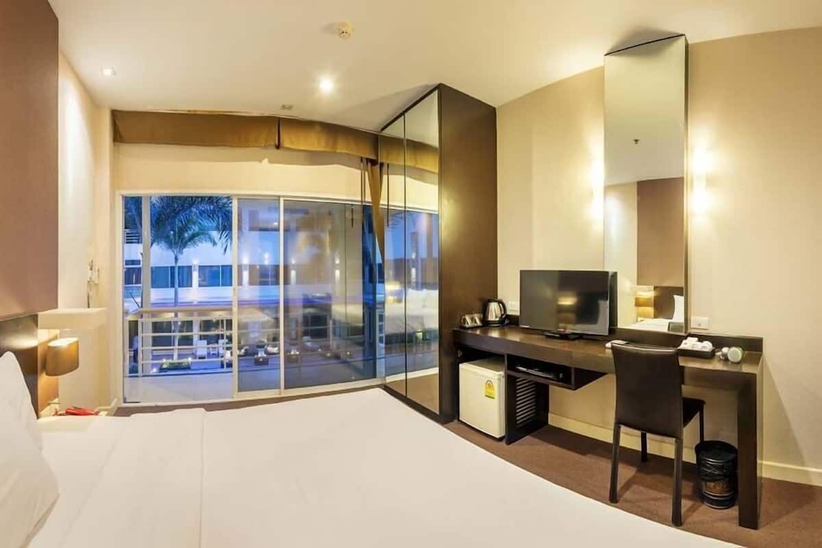 Habitación de hotel con cama, escritorio, silla, televisor y un ventanal con vistas al exterior.