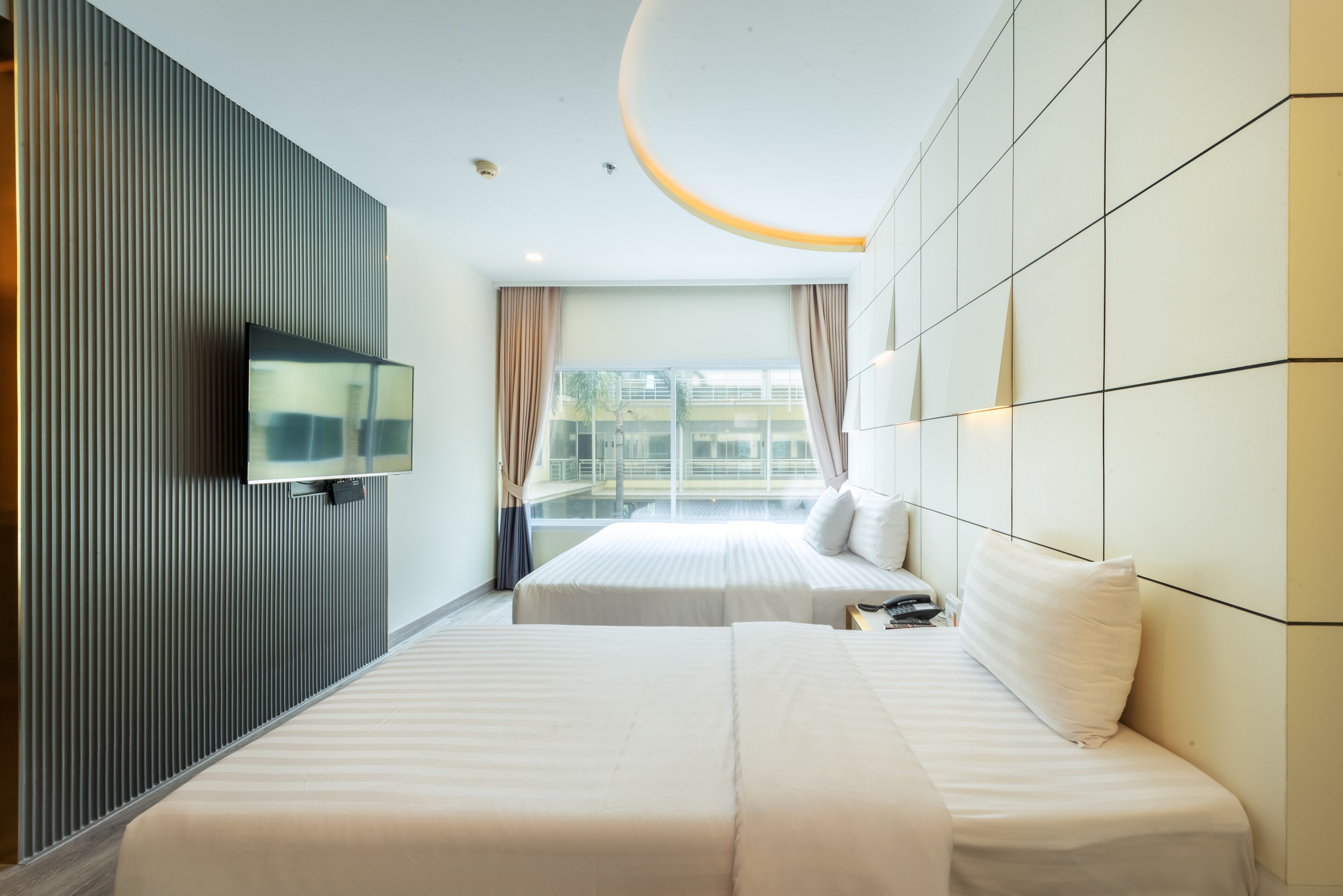Una habitación de hotel con dos camas, un televisor montado en la pared y un ventanal con cortinas.