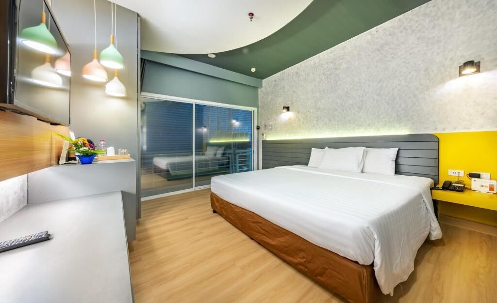 Et moderne hotelværelse med en stor seng, et skrivebord, en stol og en balkon med udsigt.
