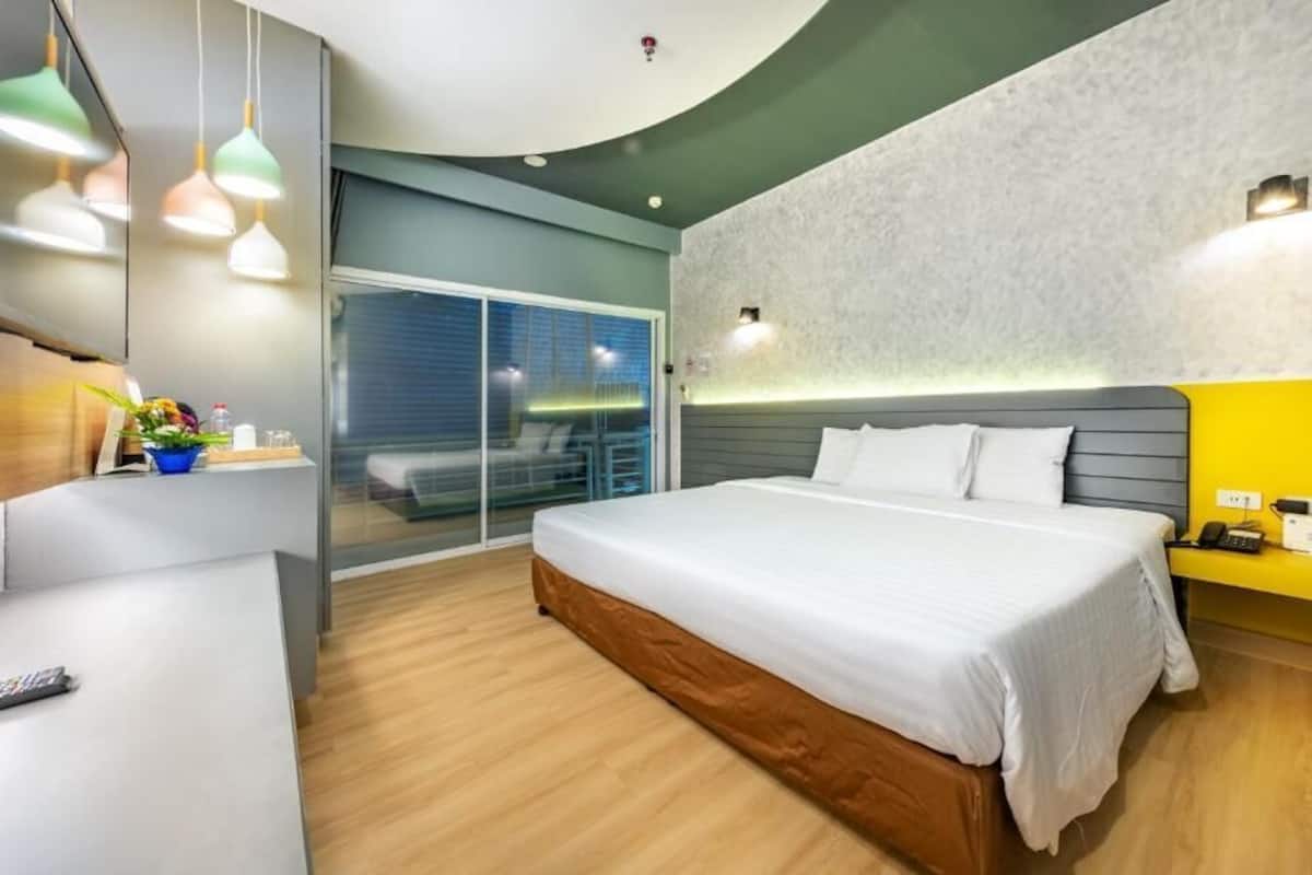 Una habitación de hotel moderna con una cama grande, un escritorio con una silla, un balcón con vistas y un baño con ducha e inodoro.