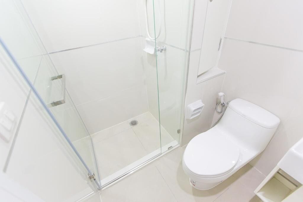 A bathroom with a glass-enclosed shower, a white toilet, and a small shelf with toiletries.