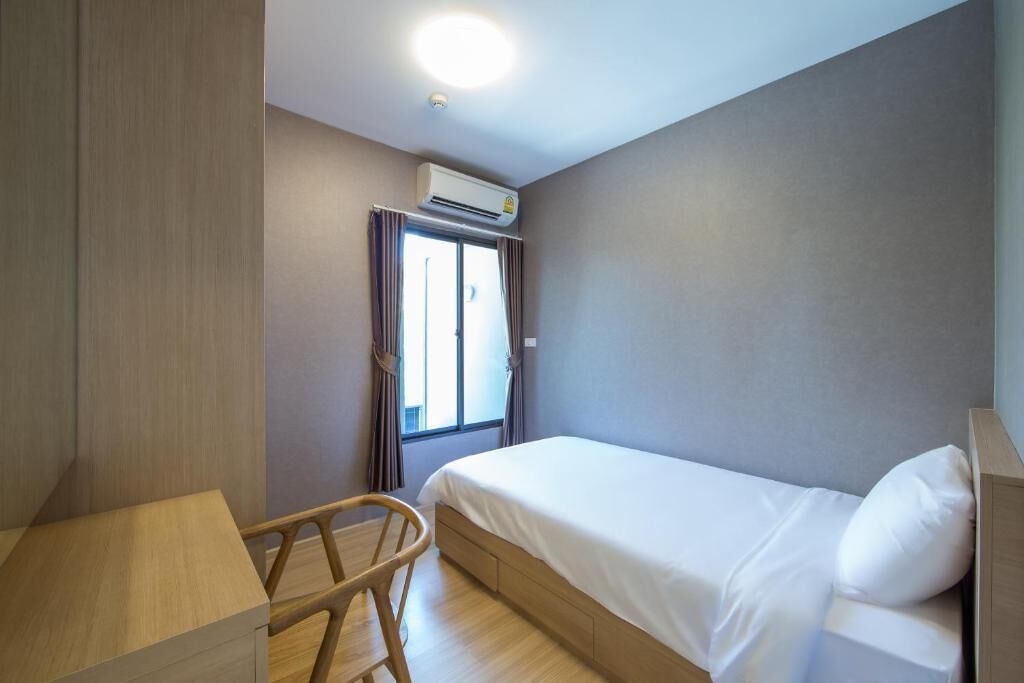A small, modern hotel room with a single bed, a wooden desk, and a chair.