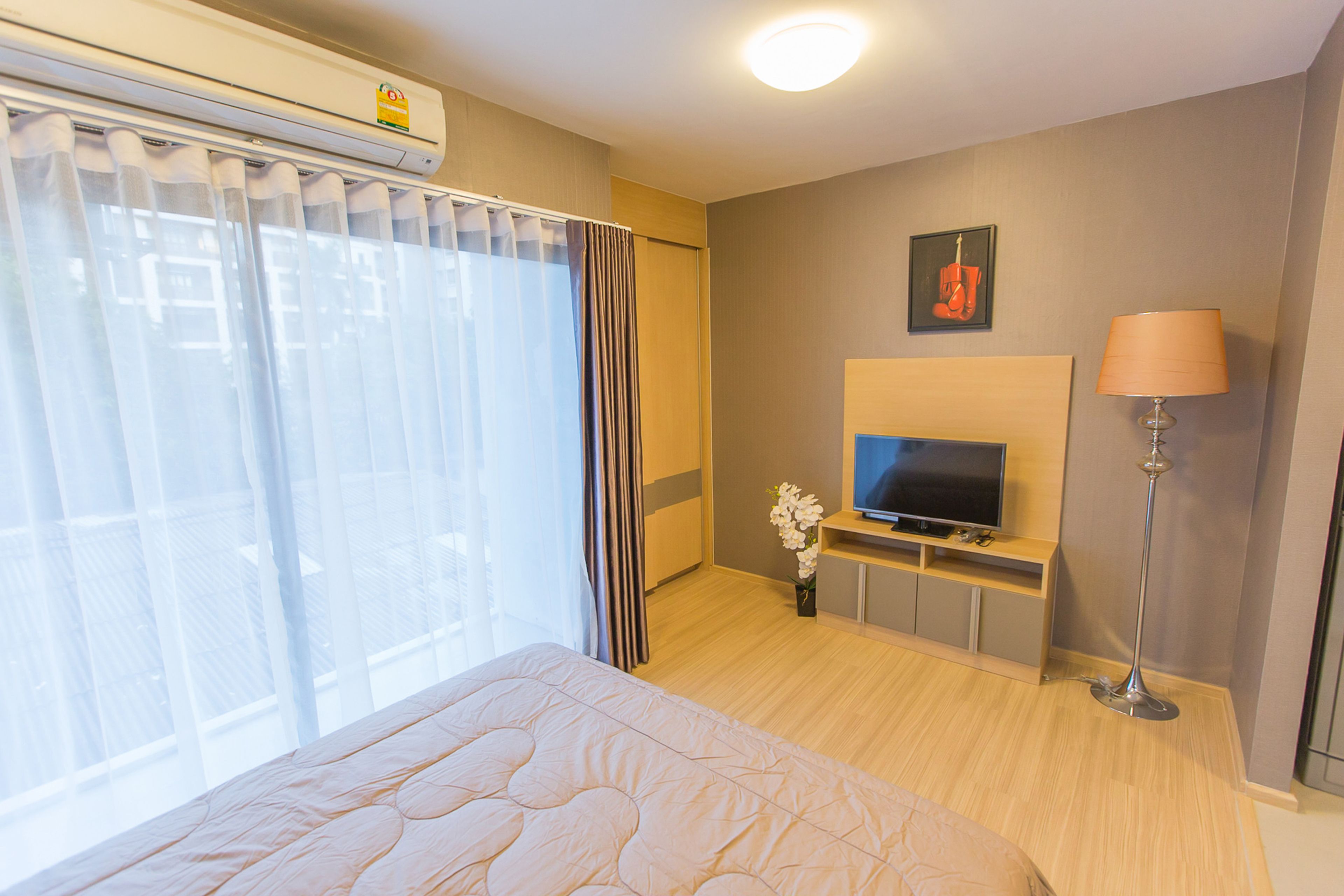 A hotel room with a bed, a TV, a lamp, and a window with curtains.