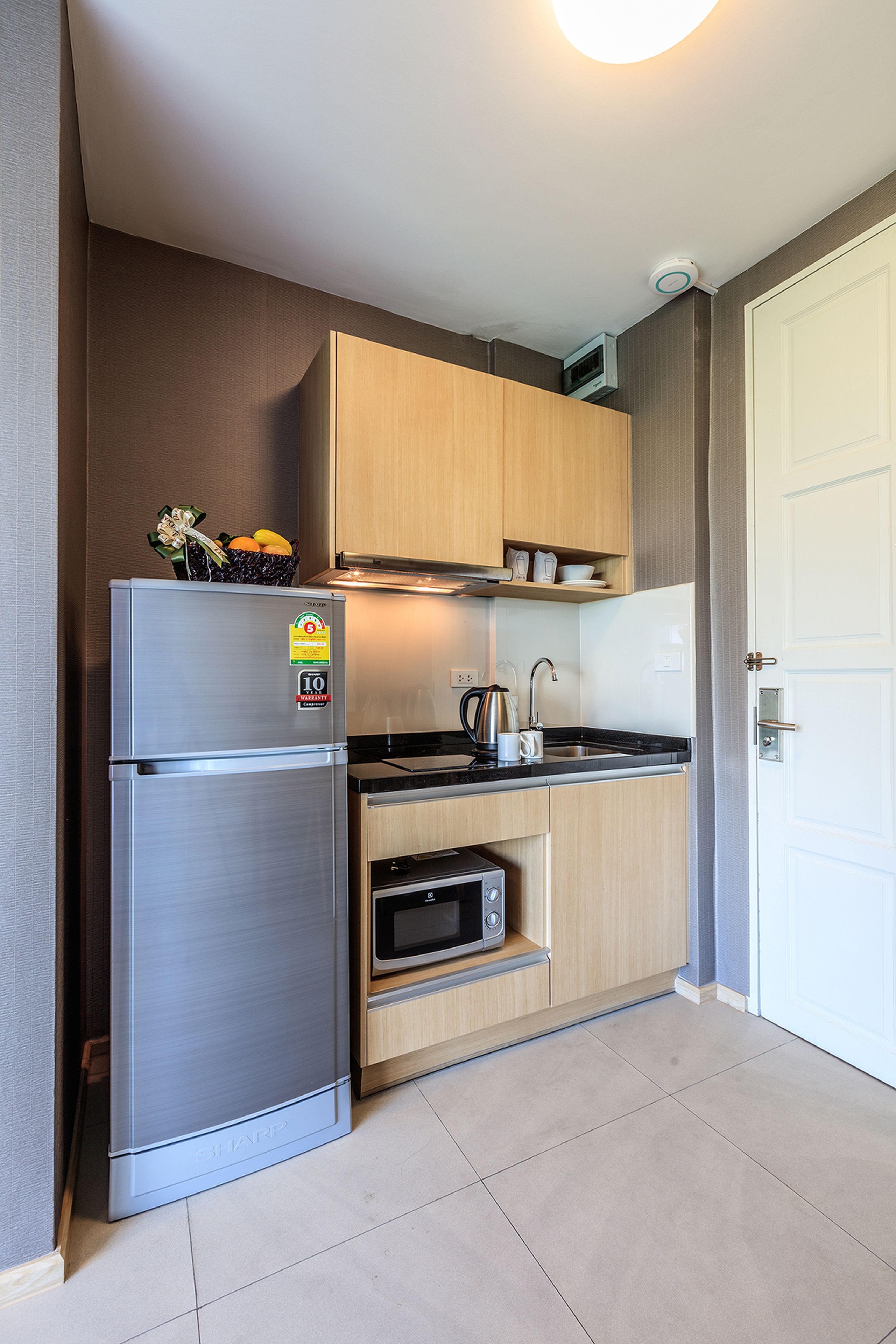 A compact kitchen with a stainless steel refrigerator, a microwave, and a kettle on the countertop.