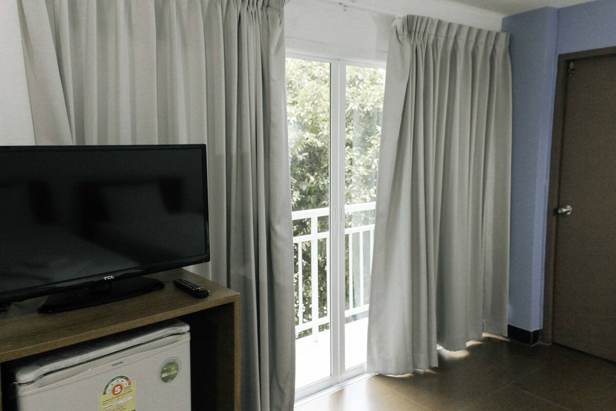 Ein Zimmer mit Flachbildfernseher auf Holzfuß, einer kleinen Kühlbox und einer Glastür zum Balkon.