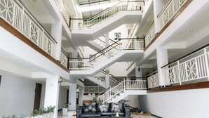 Ein mehrgeschossiges Atrium mit einer zentralen Treppe, weißen Geländern und einer Sitzecke mit schwarzen Sofas.