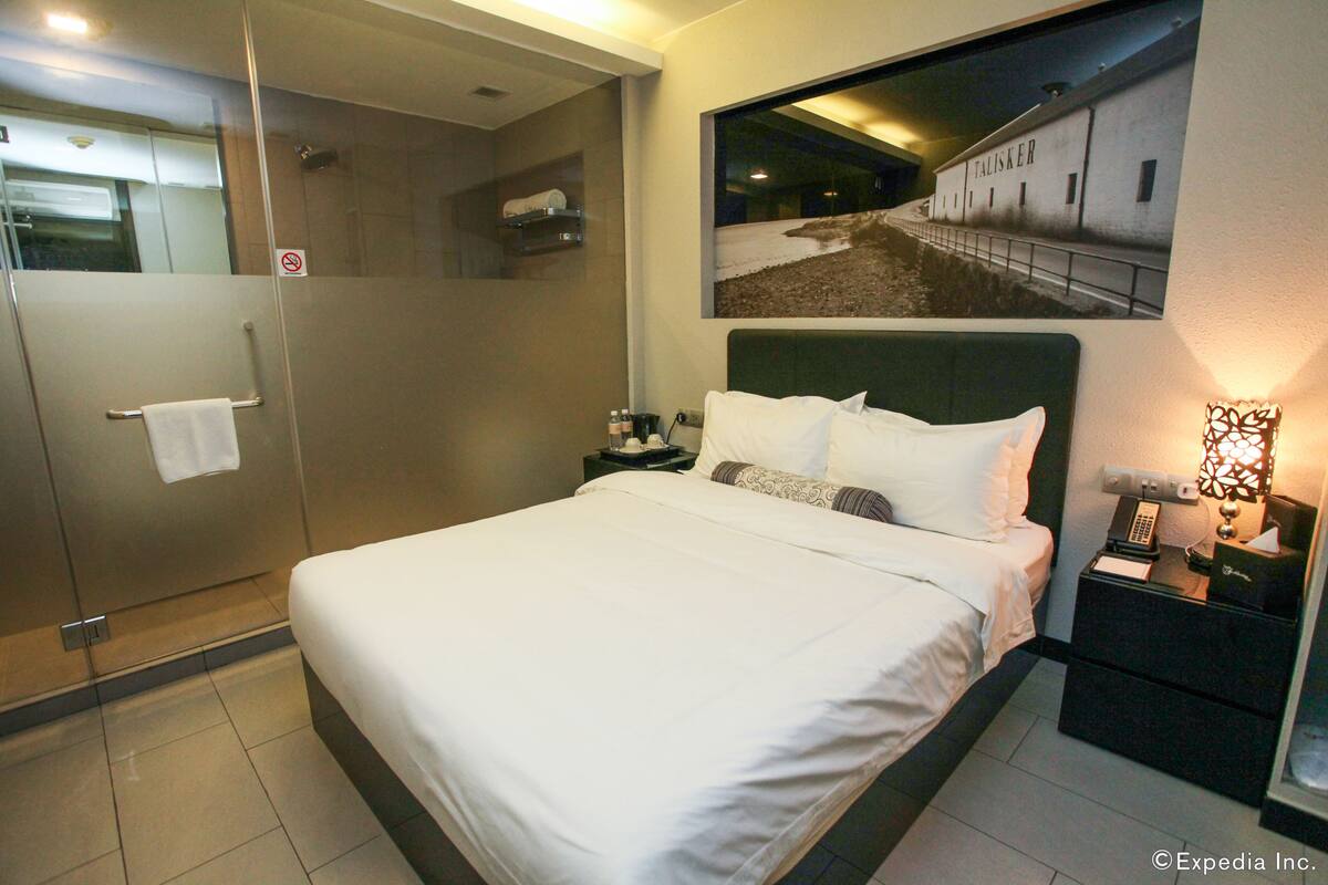 Habitación de hotel con una cama grande, una mesita de noche, un cuadro en la pared y una zona de ducha.