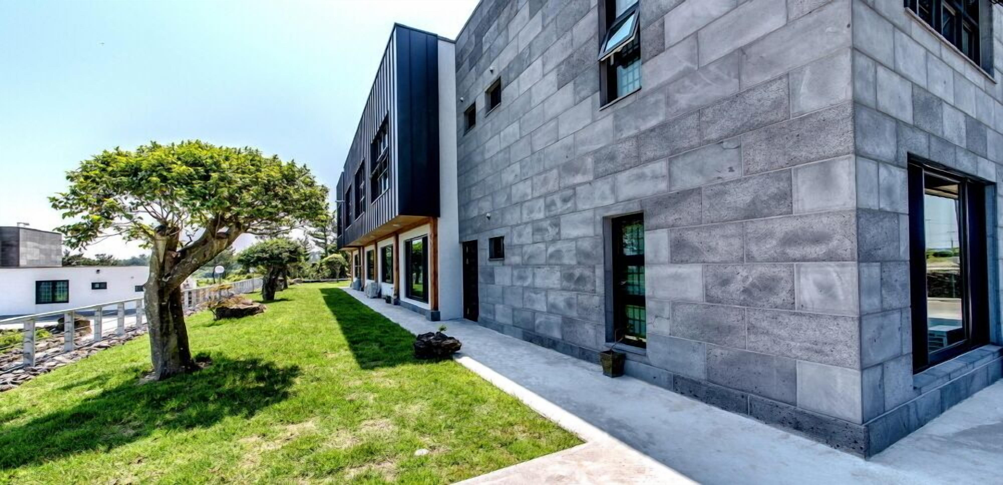 Un edificio moderno con fachada de piedra, ventanas grandes y un césped cuidado con un árbol.
