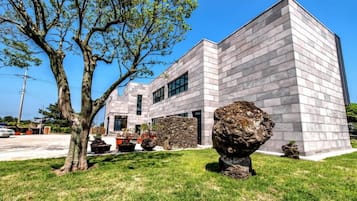 Un edificio moderno con fachada de piedra, un árbol grande en primer plano y un coche aparcado cerca.
