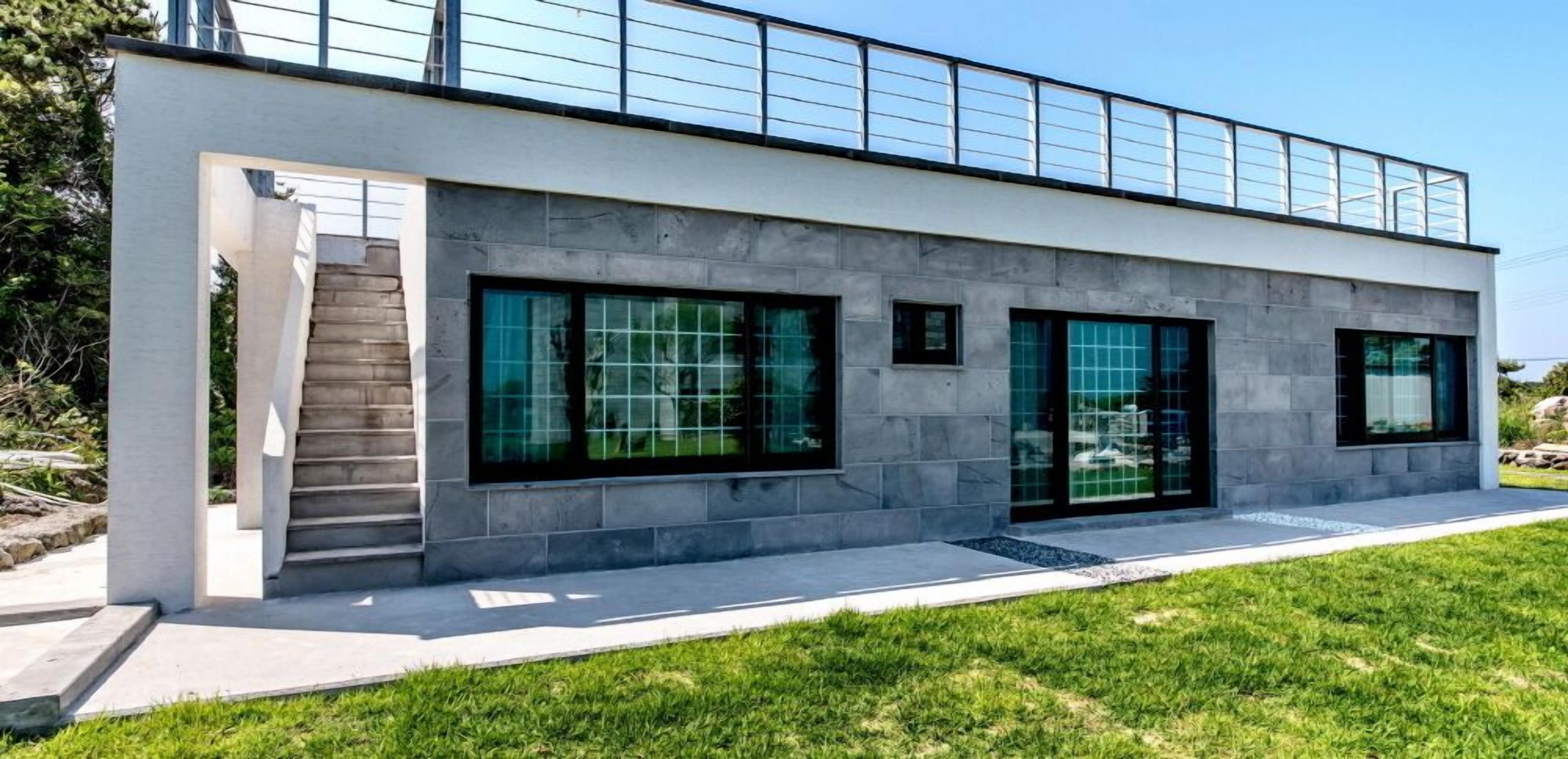A modern building with a flat roof, large windows, and a staircase leading to an upper level.