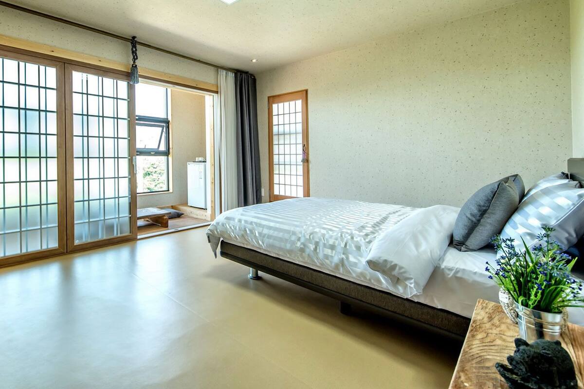 A spacious bedroom with a large bed, a wooden nightstand, and a view through a sliding glass door.