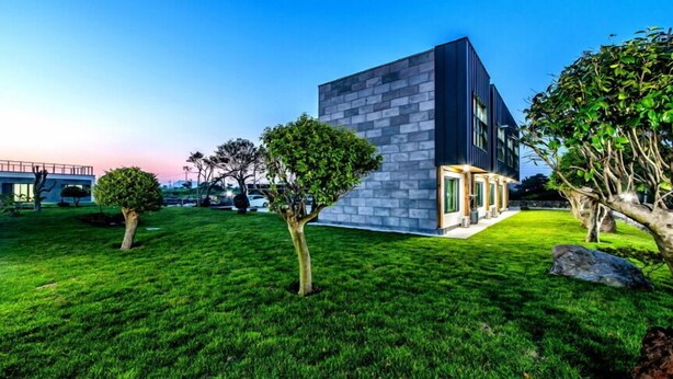 Un edificio moderno con fachada de piedra, rodeado de césped y árboles bien cuidados.