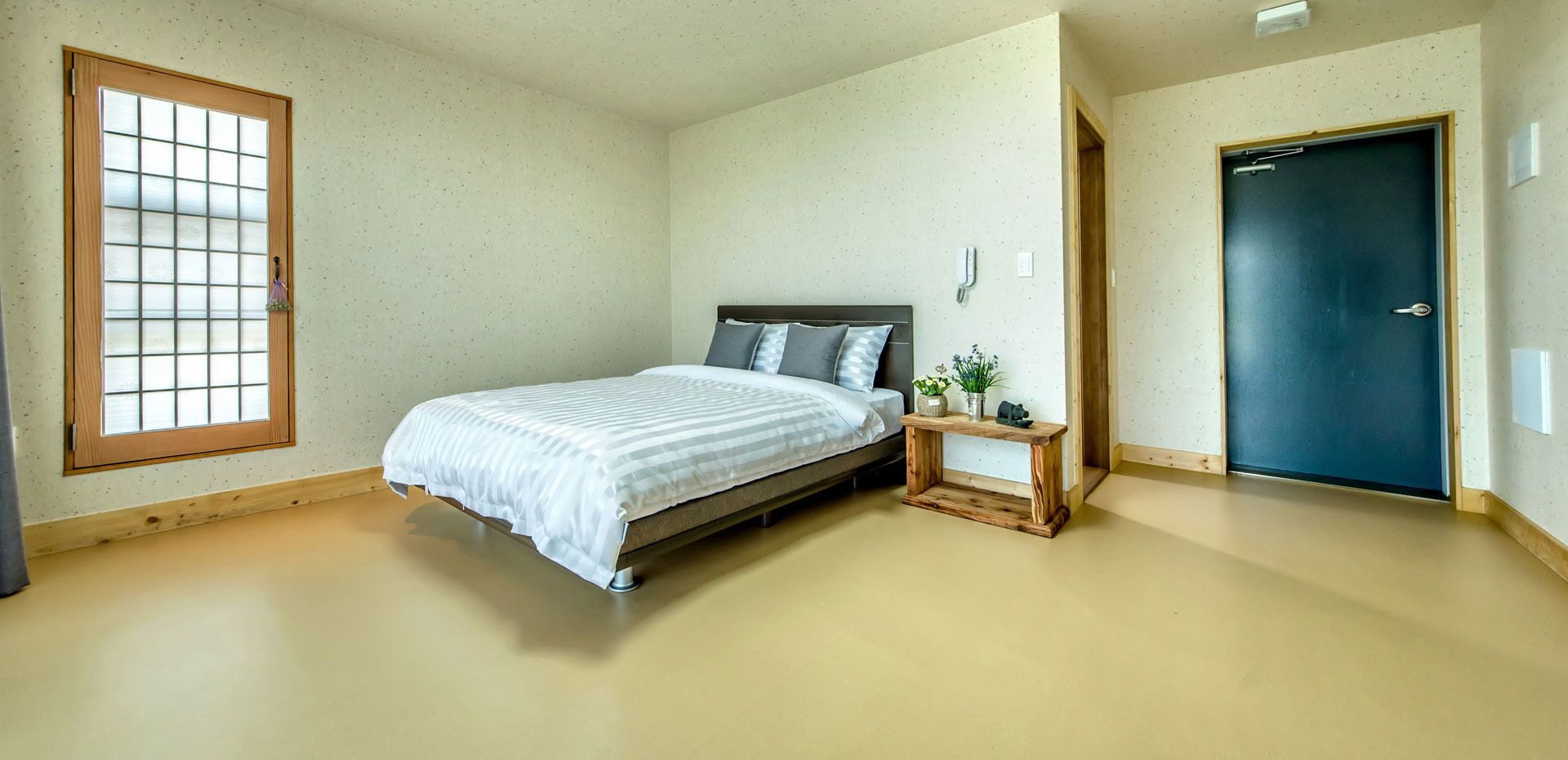 A bedroom with a bed, a small wooden nightstand, a window, and a door.