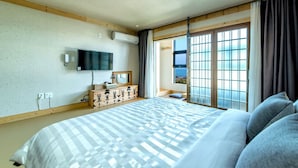 Habitación de hotel con una cama grande, un aparador de madera, un televisor de pantalla plana y vistas al mar a través de un biombos shoji.