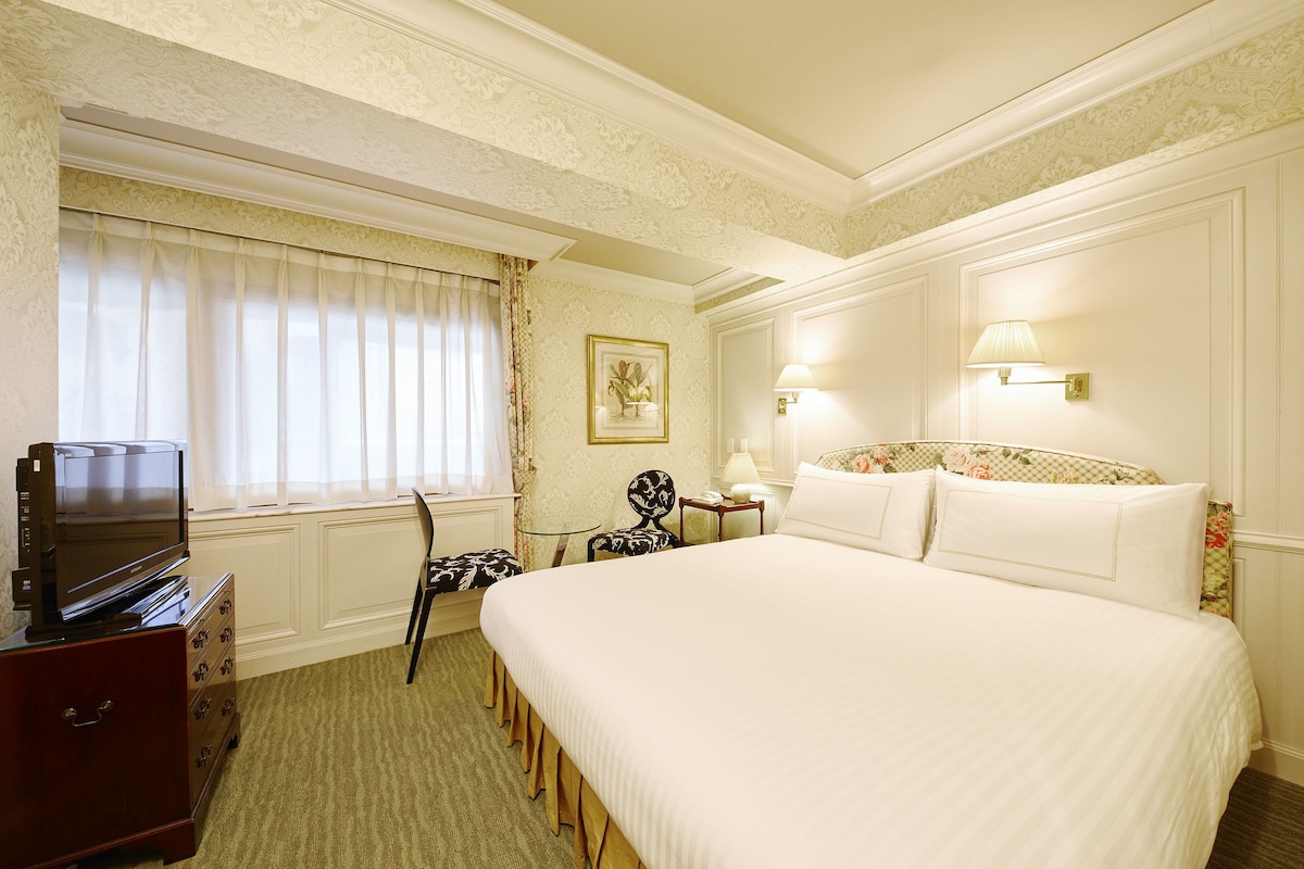 Habitación de hotel con una cama grande, un televisor sobre una cómoda, una silla, un escritorio y una lámpara.
