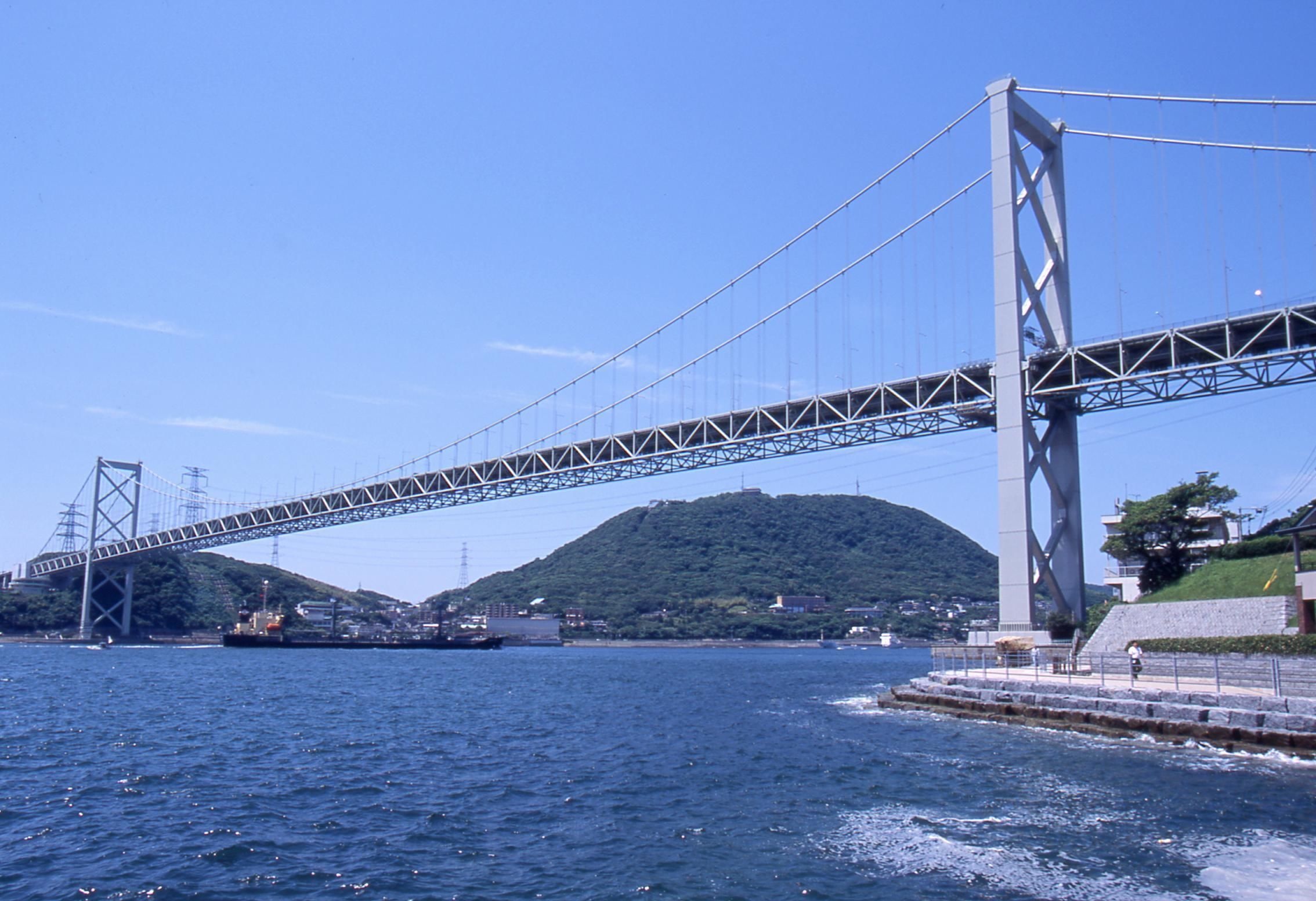 Un puente colgante grande sobre un cuerpo de agua, con un paisaje montañoso al fondo.