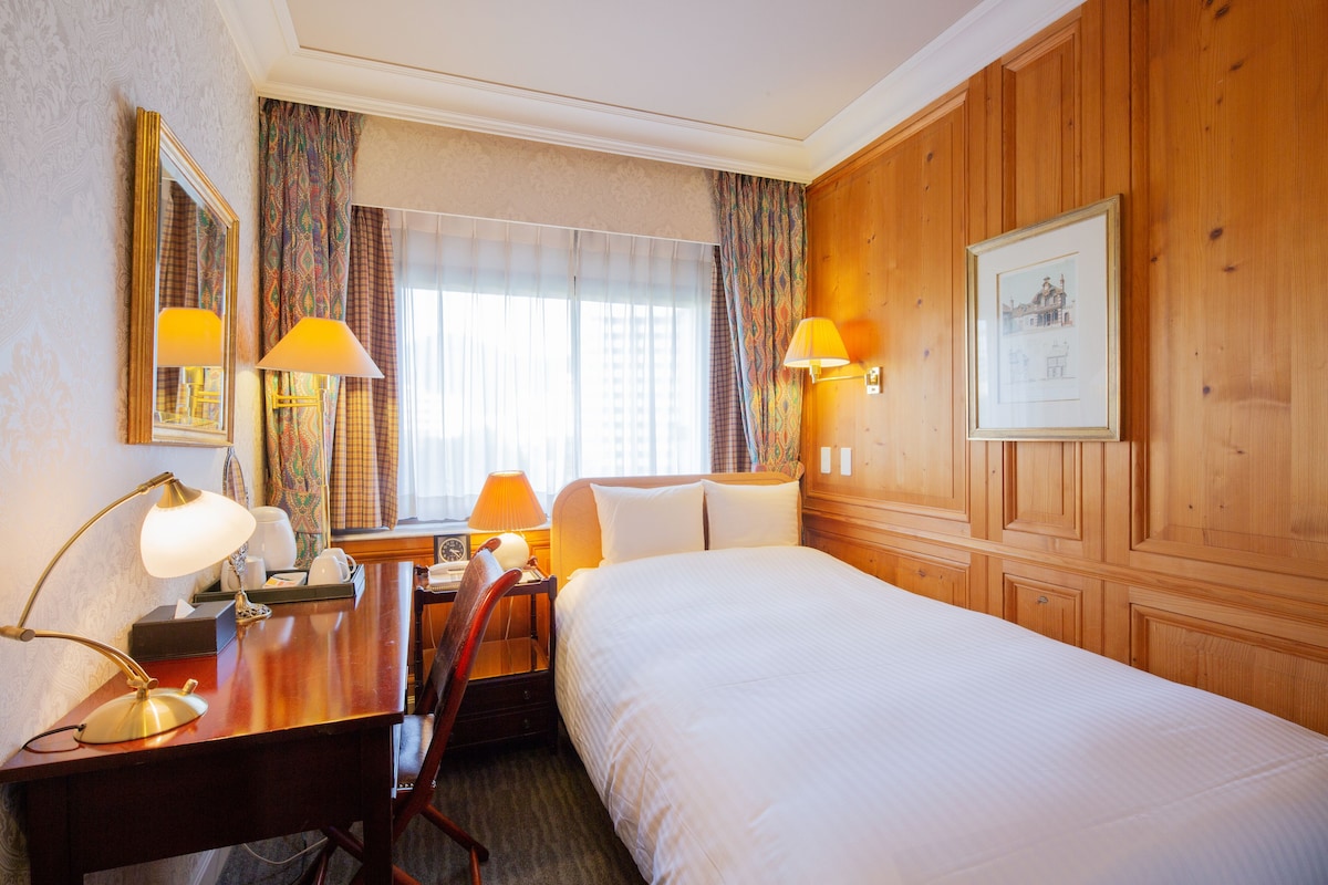 Habitación de hotel con una cama grande, dos lámparas de noche, un cabecero de madera, un cuadro enmarcado en la pared y un escritorio con una lámpara.