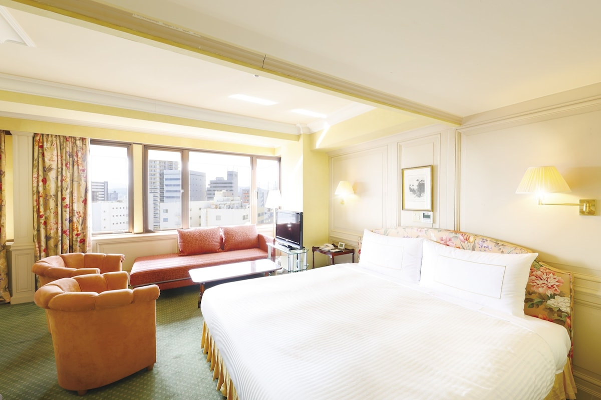 Una habitación de hotel con una cama grande, un sofá, un televisor y vistas a la ciudad.
