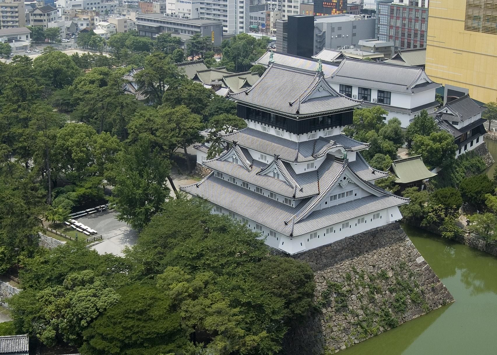 A traditional Japanese castle with multiple tiers, surrounded by lush greenery and a moat.