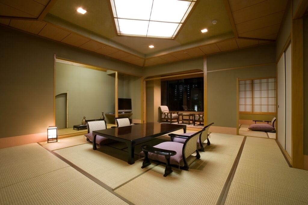 A traditional Japanese room with tatami flooring, a low table, cushioned seating, and sliding doors.